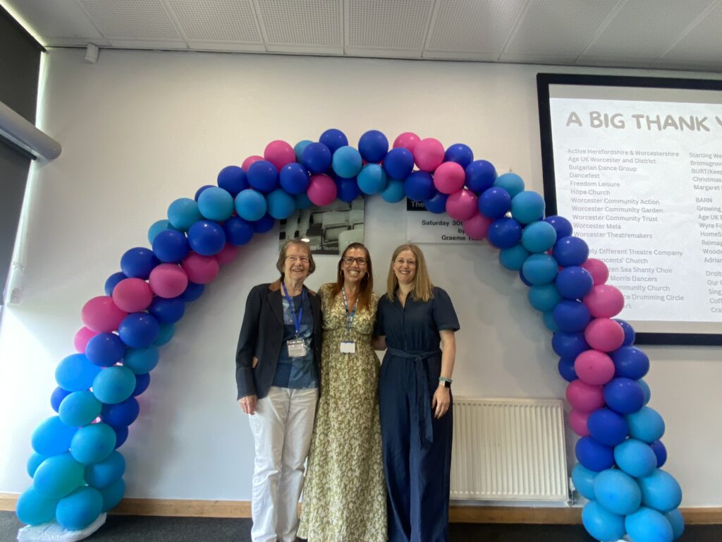 3 event attendees stood under a balloon arch