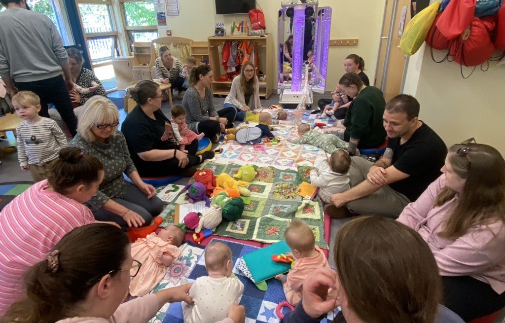 people sat around a soft mat with their babies on the mat